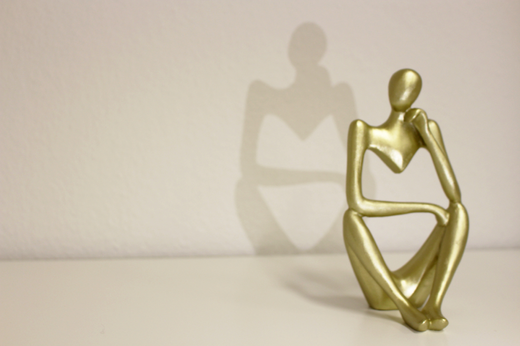 Goldene Skulptur eines nachdenklichen Menschen mit einem Schatten